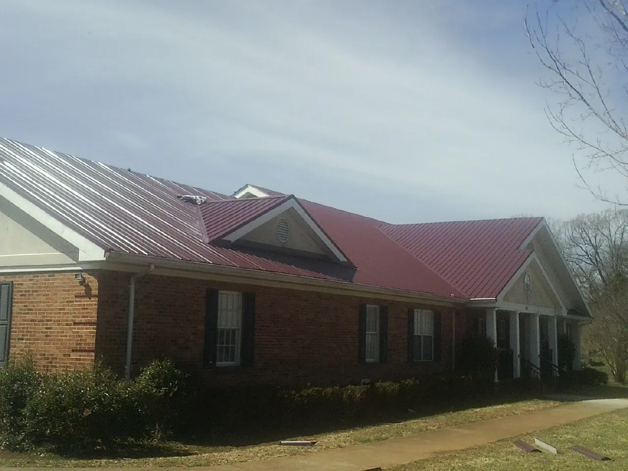 Red metal roof with gabled entries on a long brick building, from a Hail Damage Roof Repair job in Chula Vista
