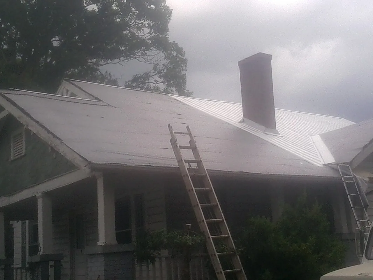 Ladders against a metal roof on an older home with a brick chimney in Chula Vista