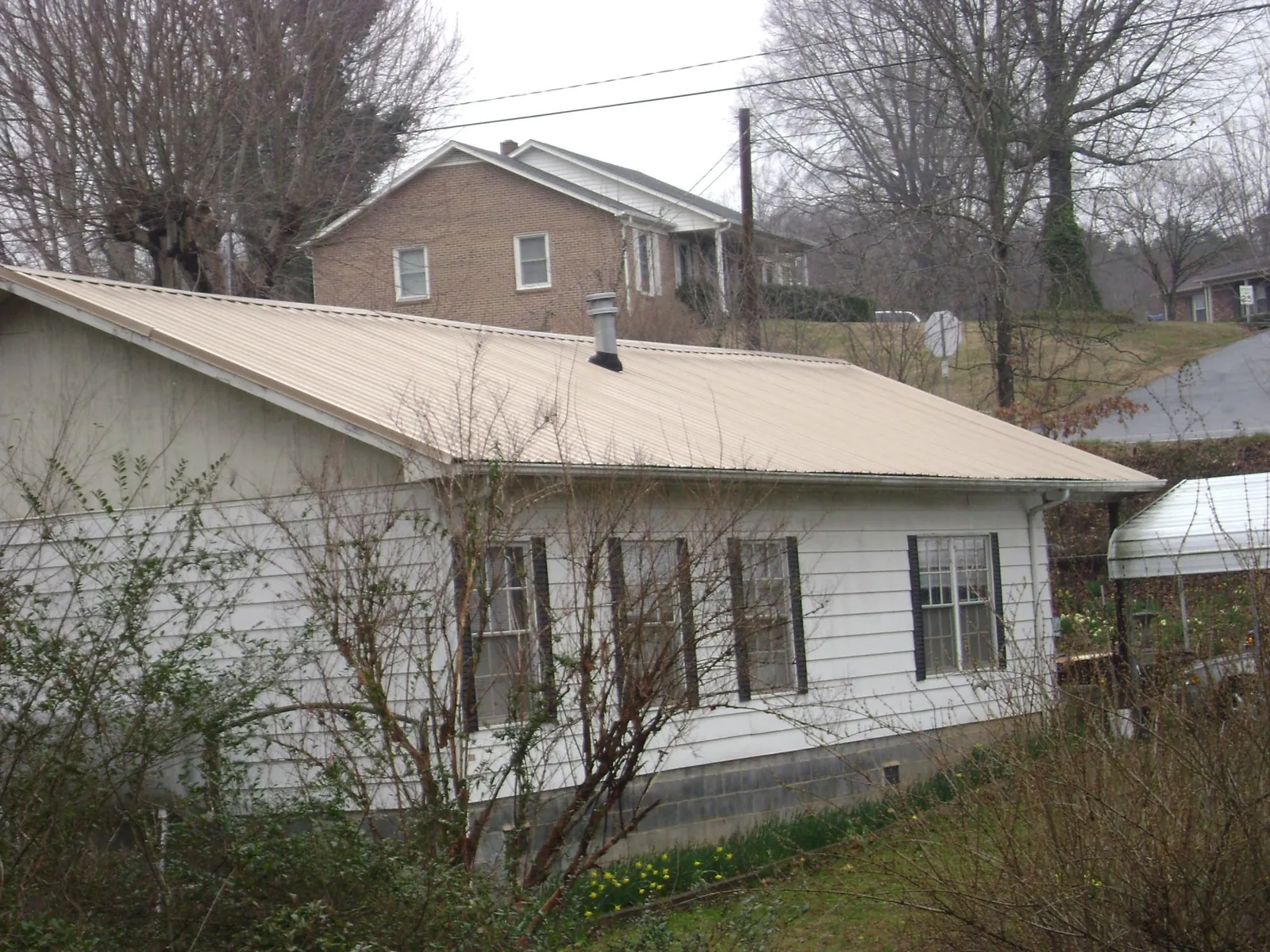 Tan metal roof on a white sided house set into a hillside — Commercial Roofing by Roofing Brothers in Chula Vista